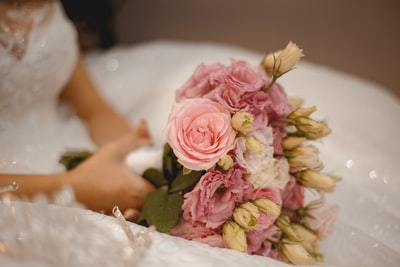 女人穿着白色婚纱拿着粉红色和白色的花朵的花束

